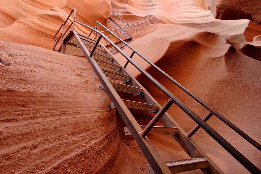 Image shows a metal staircase set into wavy red sandstone.