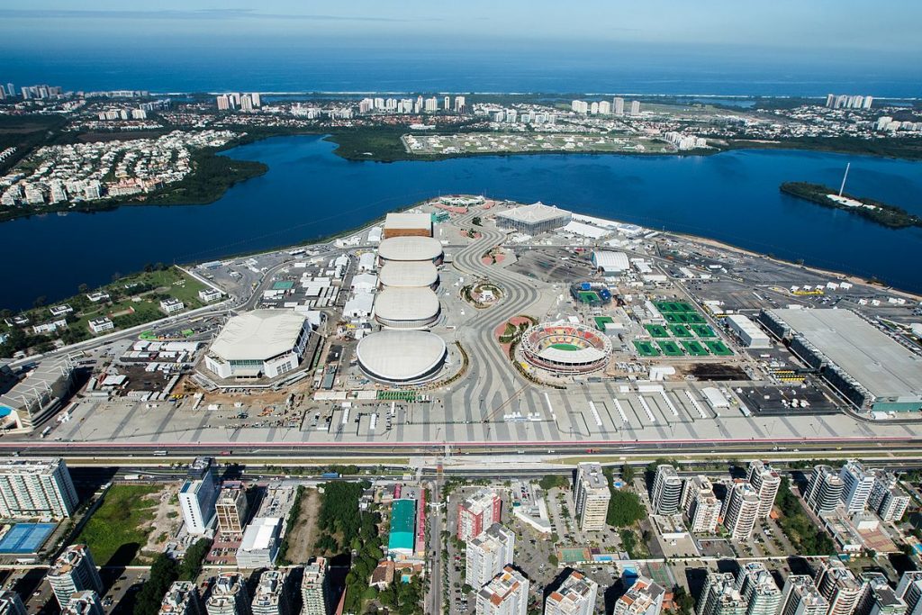 Image overlooks Olympic Park, with the several arenas, stadiums, tracks, courts, and buildings. It juts out into the lagoon in a triangular bit of land. Beyond is another strip of land heavily built up, and then the bay.