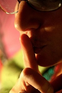 Photo of lower half of face with finger to the mouth in a shushing gesture.