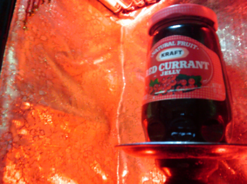A jar of Kraft Red Currant jelly sitting on a metal platform against a glowing red-orange metalic background.