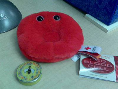 Photo of a plush red blood cell next to a blood donation sticker on a table.