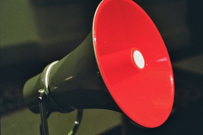 Photo of an olive green megaphone against an olive green background. Interior of megaphone is bright red.