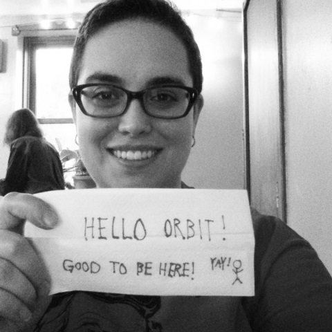 A black and white self-portrait of moi, holding a napkin with the words "Hello Orbit! Good to be here!" scrawled on it. Oh and a stick figure shouting "Yay!"