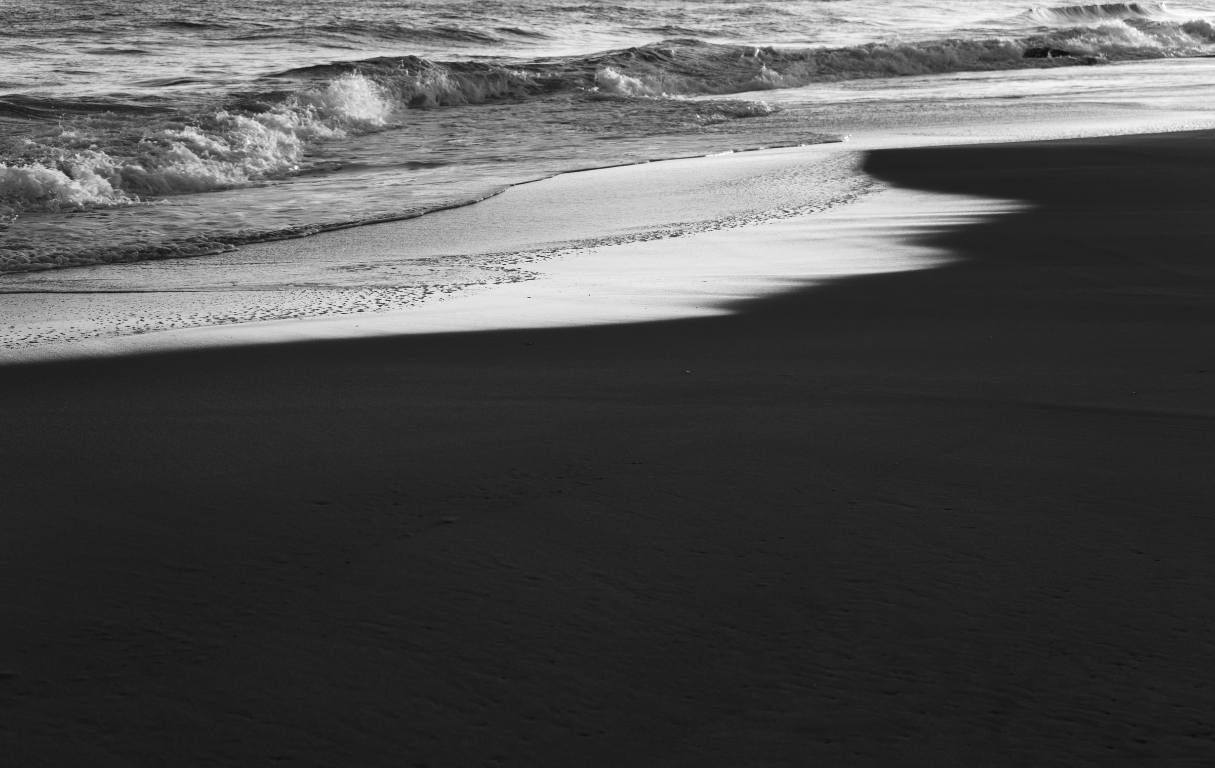 Grayscale photo of waves on a beach.