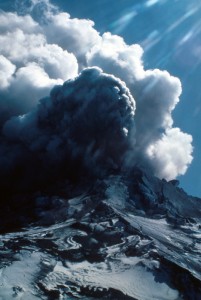 Image is taken on the slopes of Mount St. Helens, looking towards the summit, which is enveloped in clouds of ash and steam.