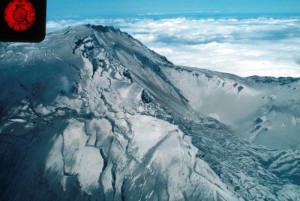 Color aerial image of Mount St. Helens shows the summit crater, which has chewed a wound in the mountain. Cracks along the high left rim show where it's being widened.
