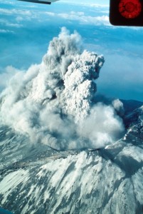 Image shows a plume of ash and steam rising from the crater of Mount St. Helens in an aerial photo.