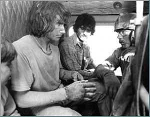 Image shows two bedraggled men sitting in a helicopter, with a National Guardsman sitting across from them.