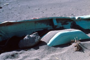 Image shows the inside of the damaged truck bed, looking toward the rock. Ash fills the bed and covers the wheel well. There is a dacite rock about half the size of the wheel well beside it.