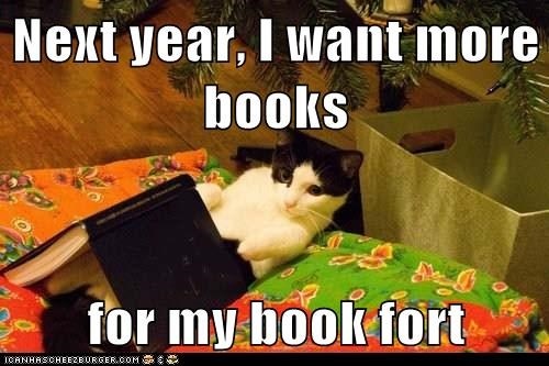 Image shows a cat lying under an Xmas tree with a book tented over it. Caption says, "Next year, I want more books for my book fort."