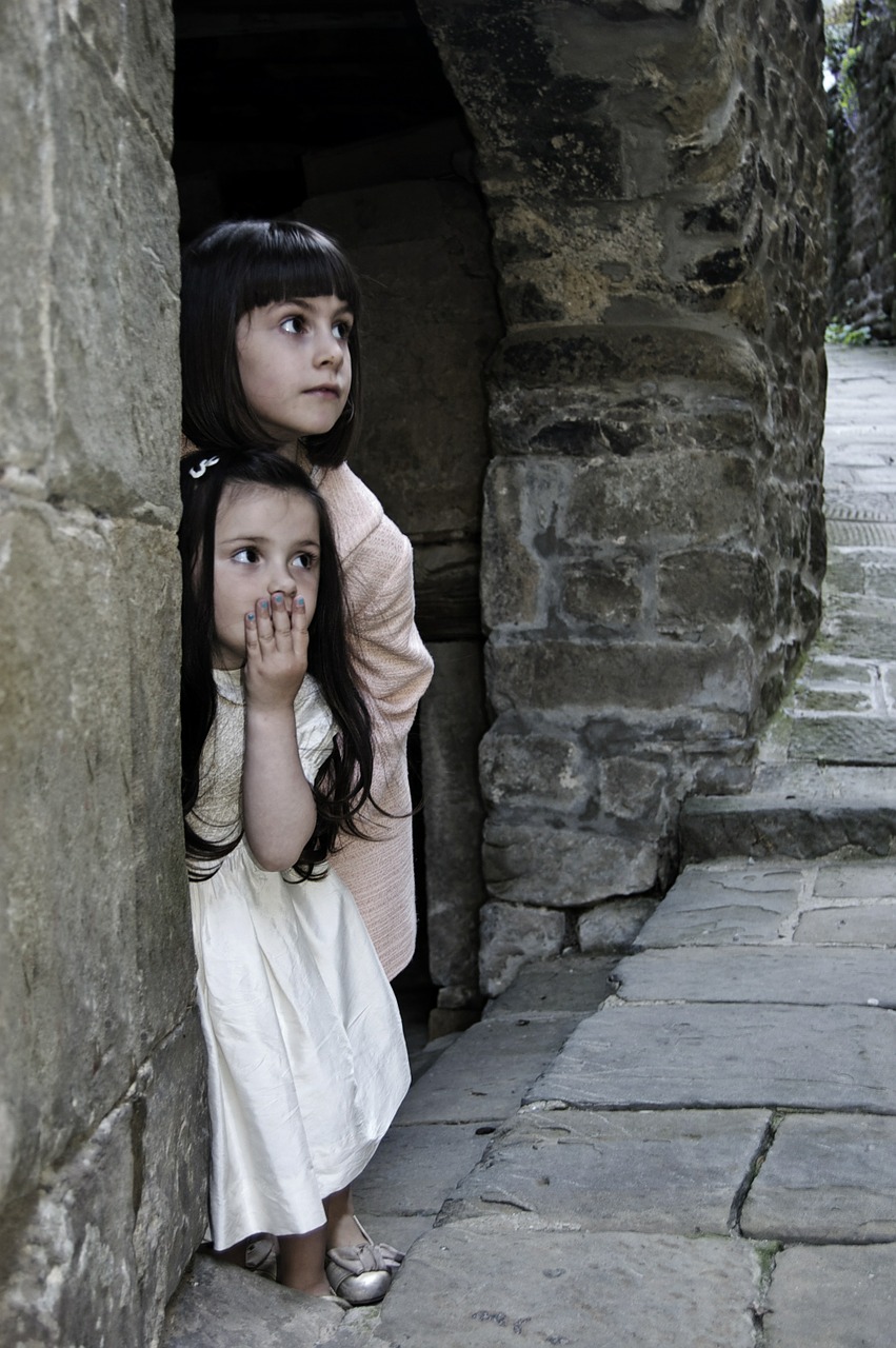Image shows a boy and girl peering fearfully from the doorway of a stone house.