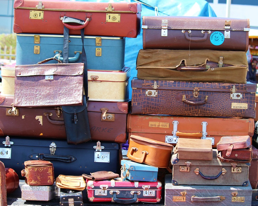 Image shows several piles of small suitcases and other luggage in assorted colors and fabrics.