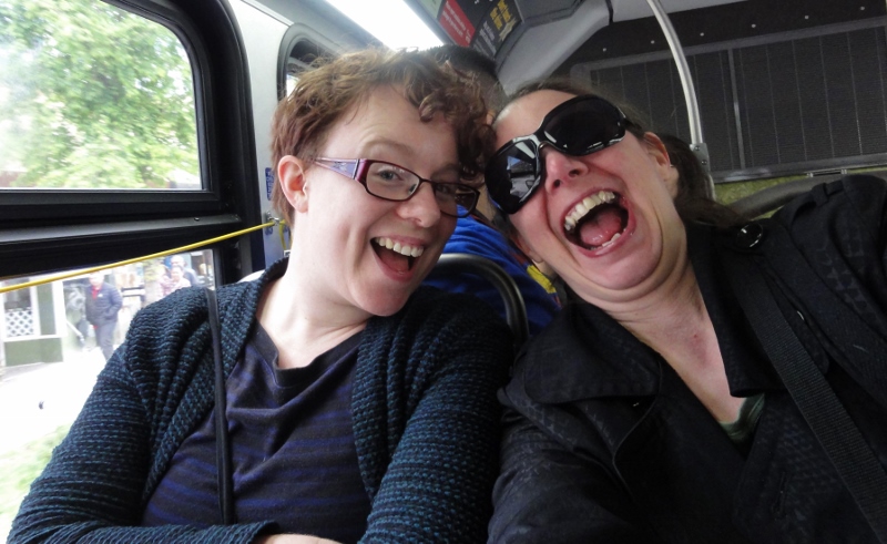 Image shows Aoife and I sitting in a bus seat, with the window behind us. We are leaning our heads together and have exaggerated grins.