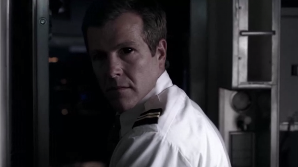 Screenshot shows a white man in a pilot's uniform, looking over his shoulder as he goes back to the cockpit. His eyes are solid black. Freaky!