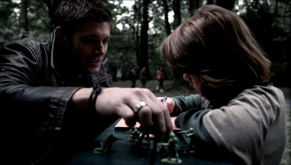 Image shows Dean crouching in front of Lucas, who's drawing. Dean is reaching for one of Lucas's army men.