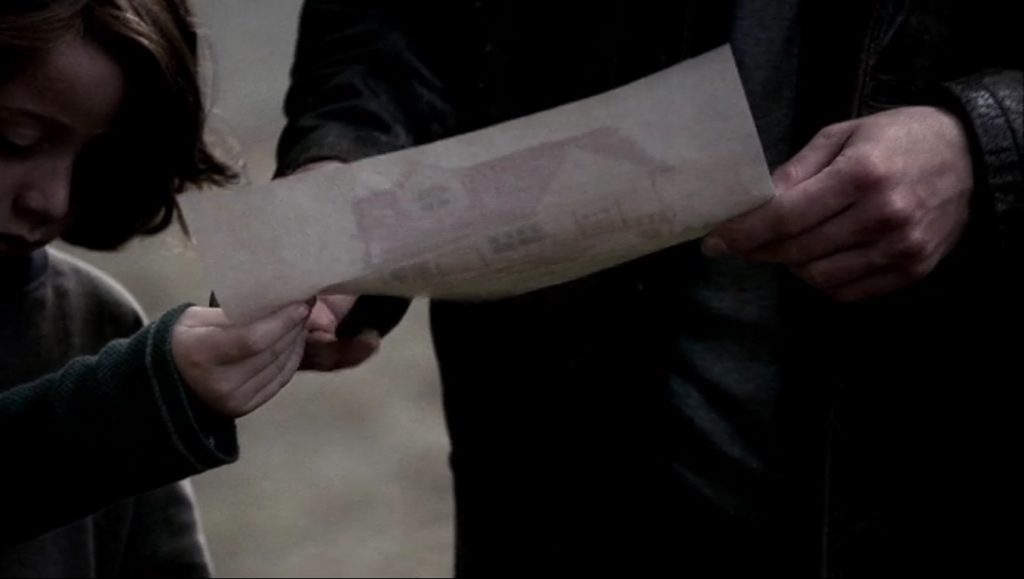 Screenshot shows Lucas handing a drawing to Dean. Only part of Lucas's face, with his eyes downcast under his long hair, is visible. All that can be seen of Dean is his hands and part of his torso. The camera is down low, pointing slightly up, so only the back side of the drawing is visible, but the light is coming through it and allowing us to see there's a house.