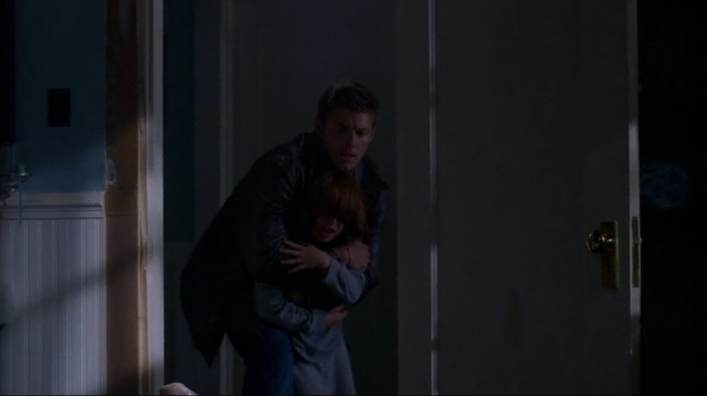Screenshot shows a bathroom door, looking into a hall. Dean and Lucas are visible. Dean has Lucas wrapped in his arms, holding him back as he struggles.