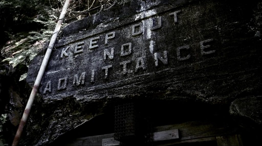 Image shows the top of the entrance to an old mine shaft. KEEP OUT NO ADMITTANCE is carved in big block letters over the door.