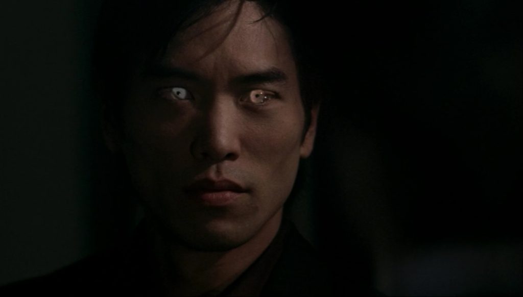 Screenshot shows the face of an East Asian man with a grim expression and the flashy yellow eyes. 