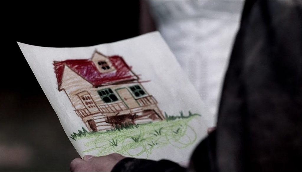 Screenshot shows a child's crayon drawing of a house with a single gable, a porch with two sets of steps, and a peaked roof, surrounded by an unkempt grassy lawn. He's used brown for the walls and red for the roof.