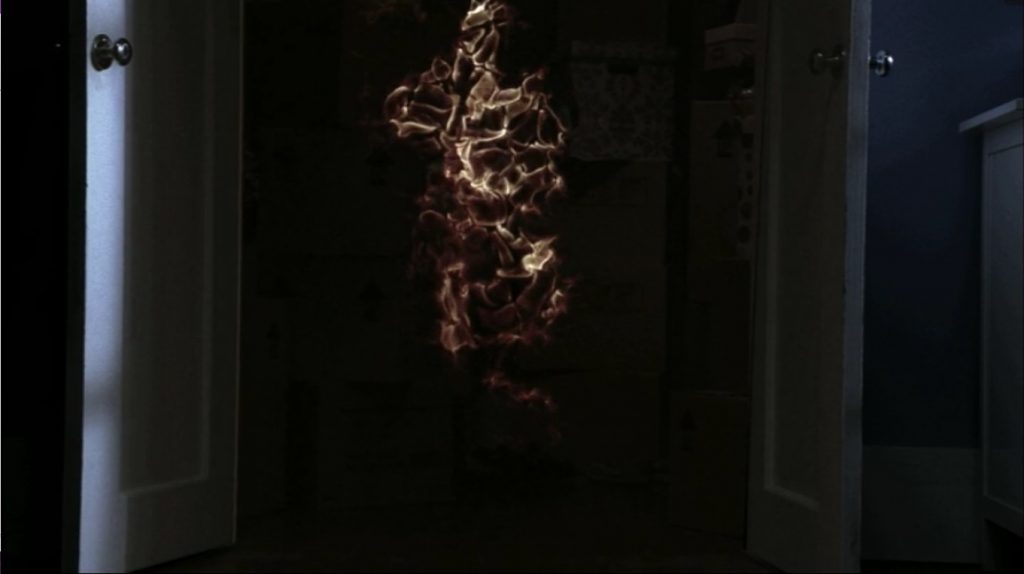 Image looks into a dark closet, the two white doors wide open. A vaguely human-shaped pillar of flame stands within.