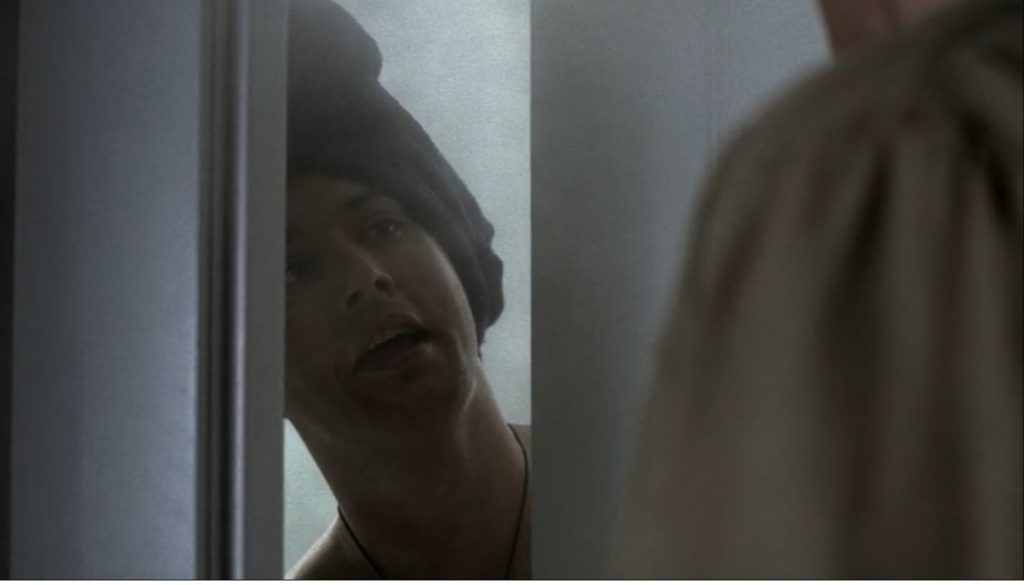 Image shows Dean from the neck up, surrounded by steam, head wrapped in a towel, grinning as he peers through a partially-opened bathroom door. Sam's shoulder is visible in the right of the frame.