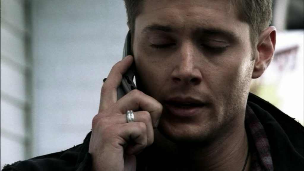 Screenshot shows Dean holding a flip-phone to his ear. His eyes are closed, and it's obvious he's on the verge of crying.