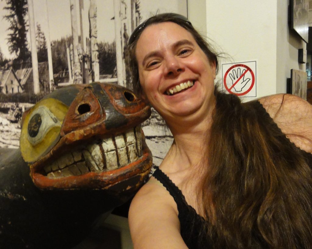 Image shows a selfie of me with a painted totem sea lion, It has the cheesiest grin of all time.