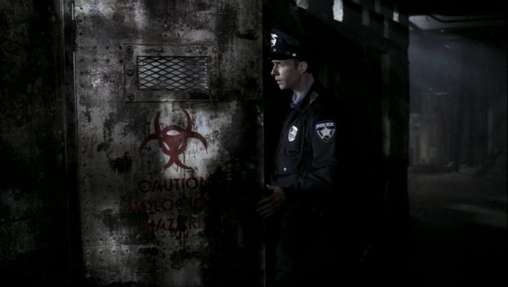 Screenshot shows a white cop with a hat with a badge on it. He's going through a dirty old metal door with a small rectangular grate near the top. Just beneath the grate is a painted red radiation symbol.