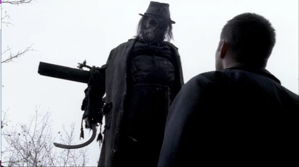 Image shows Dean looking up at a scarecrow hanging from a pole. It's got a hook for a hand, a hat that reminds me of MRAs, and a face that's between a hockey mask and a skull.