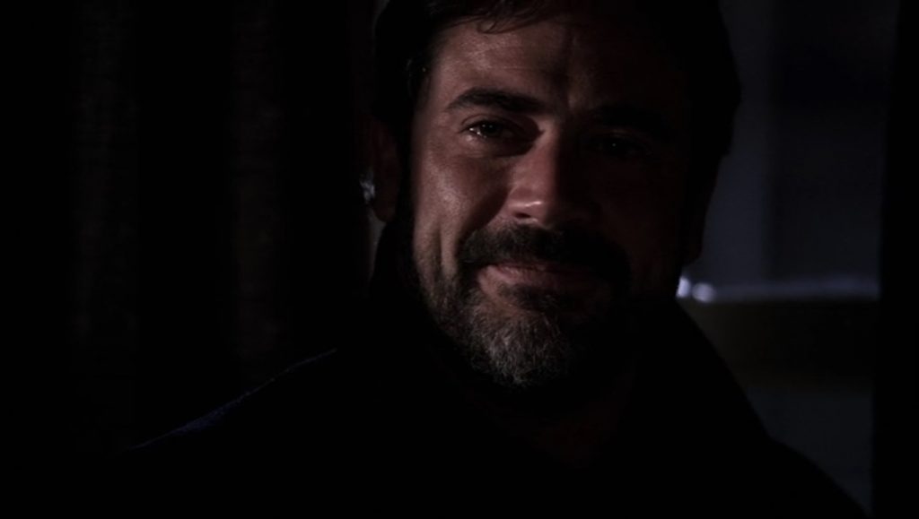 Screenshot shows John Winchester, in shadow except for his face. He has dark hair and a short, grizzled beard. His lips are pressed in a smile. There's a tear glistening in his eye.