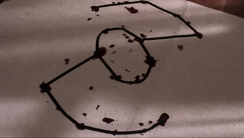 Screenshot shows a pale beige carpet with round bloodstains. Black tape connects some of the bloodstains in a symbol that looks like the arms of a Z connected in the middle by a circle. It looks a bit like an incomplete tie fighter.