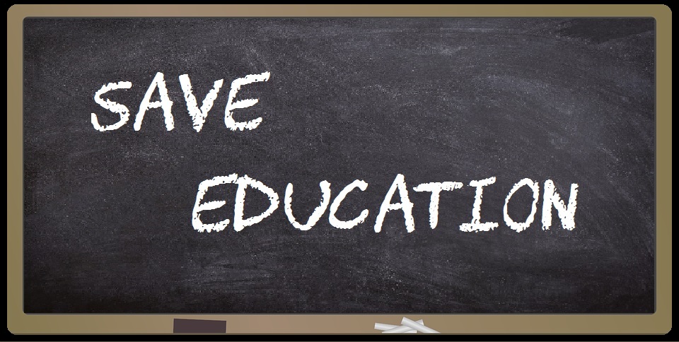 Image shows a chalkboard with an eraser and chalk on the tray. Save Education is written on the board.