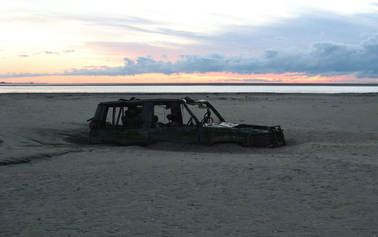 abandoned car buried halfway in sand on beach