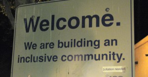 black text on white sign reading "Welcome. We are building an inclusive community." Underneath is a sticker added reading "[citation needed]"