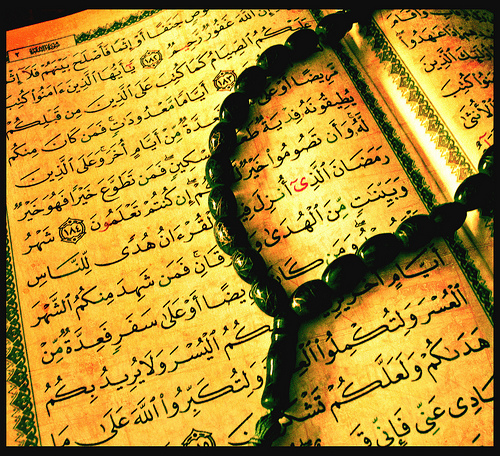 an opened copy of the Quran with prayer beads draped across it