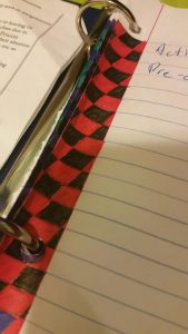 Image is of a diagonal checkerboard pattern in red and black along the edge of a loose leaf sheet of paper in a 3 ring binder.