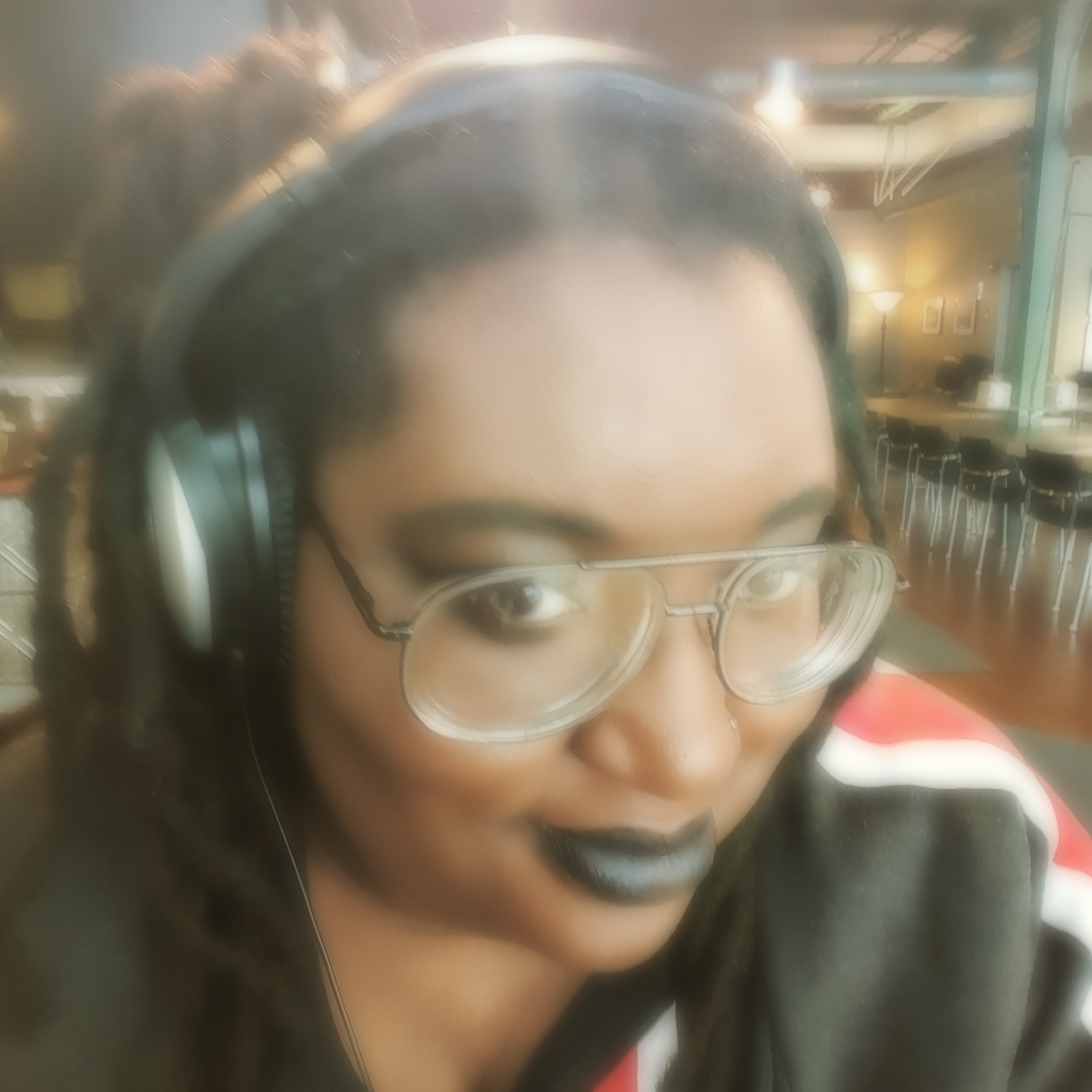 A black woman, the blog writer, upclose of her face. She is smirking, wearing a pair of large headphones and large framed glasses, with long black dreadlocks.