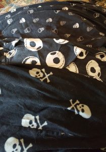Three pairs of sleep pants lay overlapping on a bedsheet. All are black with skull motifs.