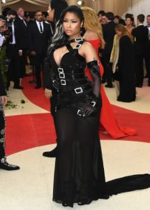 A black woman, Nicki Minaj, poses in a black dress with a sheer bottom and black buckles.